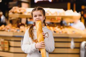 jong en grappig meisje aan het eten stokbrood in voorkant van de bakkerij op te slaan foto