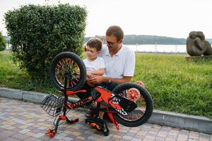 gelukkig vader en zijn zoon hebben pret samen Bij de groen park, vaststelling fiets samen. vader dag. foto