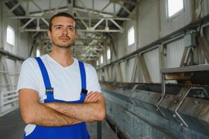 jong glimlachen professioneel in overall en beschermend helm staand in voorkant van camera binnen groot machine bouwen fabriek foto