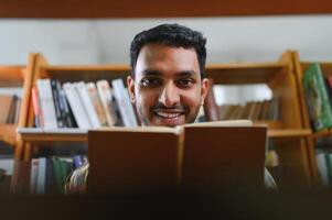 gelukkig slim Indisch of Arabisch jongen, gemengd ras mannelijk, Universiteit leerling, in de bibliotheek foto