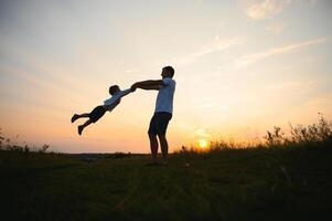 vader dag. gelukkig familie vader en kleuter zoon spelen en lachend Aan natuur Bij zonsondergang foto