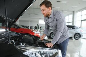 looks onder de kap van auto. jong Mens in de auto dealerschap. foto