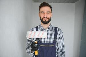 portret van knap monteur met stoppels in blauw algemeen, overhemd hebben zijn armen gekruist, op zoek Bij camera foto