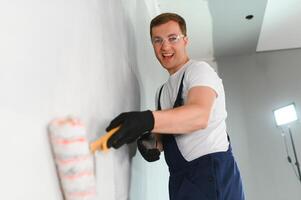 een schilder met verf rol maken muur eerste coating Bij huis reparatie vernieuwing werk. foto