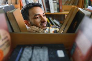 gelukkig slim Indisch of Arabisch jongen, gemengd ras mannelijk, Universiteit leerling, in de bibliotheek foto