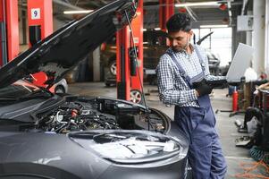 Indisch auto monteur staand en werken in onderhoud station. auto specialisten onderzoeken de opgeheven auto. professioneel reparateurs vervelend monteur uniform in blauw kleur. foto