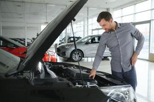 looks onder de kap van auto. jong Mens in de auto dealerschap. foto