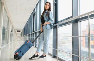 jong vrouw trekken koffer in luchthaven terminal. kopiëren ruimte foto