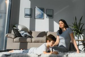 jong moeder met haar 4 jaren oud weinig zoon gekleed in pyjama zijn ontspannende en spelen in de bed Bij de weekend samen, lui ochtend, warm en knus tafereel. foto