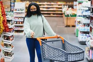 Afrikaanse vrouw vervelend beschikbaar medisch masker. boodschappen doen in supermarkt gedurende coronavirus pandemia uitbraak. epidemie tijd foto