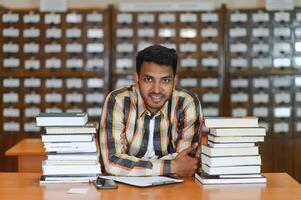 gelukkig slim Indisch of Arabisch jongen, gemengd ras mannelijk, Universiteit leerling, in de bibliotheek foto