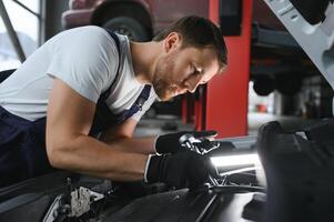 een monteur is aan het doen auto controle onder de kap met zaklamp Bij mechanica winkel. foto