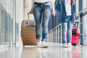 gelukkig jong moeder en haar dochter wandelen in de luchthaven terminal terwijl draag- een koffer. hoog seizoen en vakantie concept. kom tot rust en levensstijlen foto