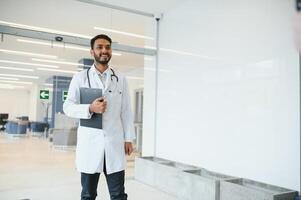 portret van mannetje Indisch dokter vervelend wit jas hebben Open deur Aan kliniek gang net zo achtergrond foto