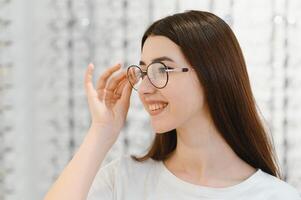 jong vrouw met bril in optisch op te slaan - mooi meisje vervelend bril in opticien winkel foto