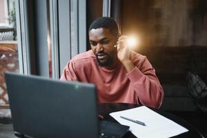 vrolijk jong Afrikaanse Amerikaans leerling Mens in hoofdtelefoons gebruik makend van computer in cafe. online video babbelen met vrienden. foto