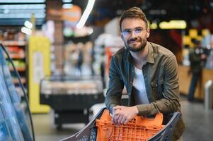 portret van glimlachen knap Mens kruidenier boodschappen doen in supermarkt, kiezen voedsel producten van plank foto