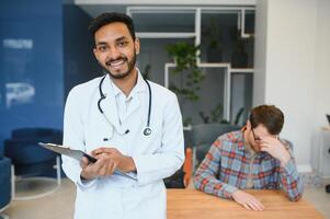 geneesmiddel, gezondheidszorg en mensen concept - Indisch dokter jong mannetje geduldig vergadering Bij ziekenhuis foto