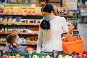 boodschappen doen met kinderen gedurende virus uitbraak. moeder en kind vervelend chirurgisch gezicht masker buying fruit in supermarkt. mam en weinig jongen kopen vers groente in kruidenier op te slaan. familie in winkel foto