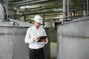 jong glimlachen professioneel in overall en beschermend helm staand in voorkant van camera binnen groot machine bouwen fabriek foto