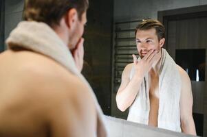 jong Mens op zoek in spiegel na scheren Bij huis foto