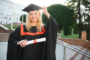 portret enthousiast vrouw college leerling afstuderen in pet en japon vieren, Holding diploma. foto