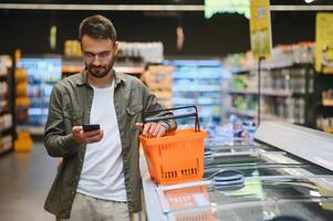 knap Mens boodschappen doen in supermarkt, glimlachend, gebruik makend van telefoon. foto