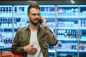 gelukkig Mens buying gezond voedsel en drinken in een modern supermarkt en pratend Aan telefoon. foto