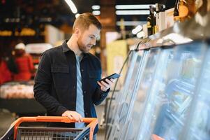 knap Mens buying sommige gezond voedsel en drinken in modern supermarkt of kruidenier op te slaan. levensstijl en consumentisme concept. foto