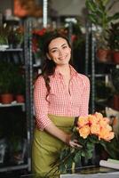 schattig meisje bloemist verzamelt een boeket van rozen in een bloem winkel. een mooi bloemist creëert een samenstelling van bloemen. meisje bezuinigingen bloemen en verwijdert muf bladeren foto