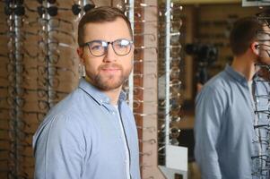 groot keuze. elegant Mens met baard kiezen bril in de optiek op te slaan. foto