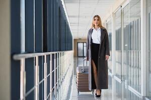 portret van geslaagd bedrijf vrouw op reis met geval Bij luchthaven. mooi elegant vrouw reizen met bagage. foto