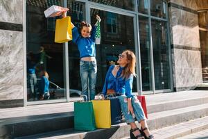 mooi mam en haar schattig weinig dochter zijn Holding boodschappen doen Tassen, op zoek Bij camera en glimlachen terwijl staand buitenshuis. boodschappen doen concept. foto