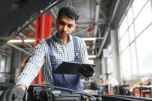 monteur Mens monteur manager arbeider gebruik makend van een laptop computer controle auto in werkplaats Bij auto auto reparatie onderhoud centrum. ingenieur jong Mens op zoek Bij inspectie voertuig details onder auto kap. foto