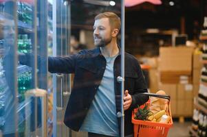 knap Mens buying sommige gezond voedsel en drinken in modern supermarkt of kruidenier op te slaan. levensstijl en consumentisme concept. foto