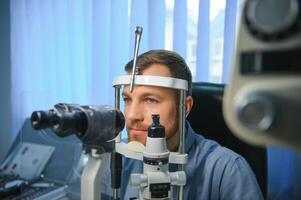volwassen Mens gezichtsvermogen test met verrekijker spleetlamp. controle netvlies van een mannetje oog detailopname. oogheelkunde kliniek foto