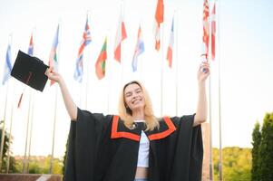 portret enthousiast vrouw college leerling afstuderen in pet en japon vieren, Holding diploma. foto