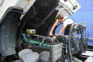 semi vrachtauto onder onderhoud. Kaukasisch vrachtauto monteur werken naar fix de tractor. foto