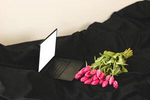 een boeket van roze bloemen Aan zwart elegant linnen met een Open laptop. foto