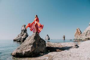 vrouw reizen zee. jong gelukkig vrouw in een lang rood jurk poseren Aan een strand in de buurt de zee Aan achtergrond van vulkanisch rotsen, Leuk vinden in IJsland, sharing reizen avontuur reis foto