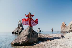 vrouw reizen zee. jong gelukkig vrouw in een lang rood jurk poseren Aan een strand in de buurt de zee Aan achtergrond van vulkanisch rotsen, Leuk vinden in IJsland, sharing reizen avontuur reis foto