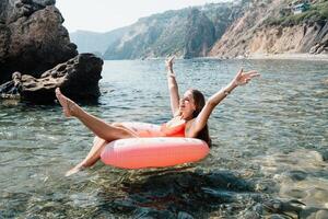 vrouw zomer zee. gelukkig vrouw zwemmen met opblaasbaar donut Aan de strand in zomer zonnig dag, omringd door vulkanisch bergen. zomer vakantie concept. foto