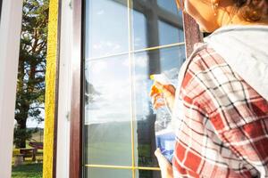 vrouw handmatig wast de venster van de huis met een vod met verstuiven schoonmaakster en dweilen binnen de interieur met wit gordijnen. herstellen bestellen en netheid in de lente, schoonmaak onderhoud foto