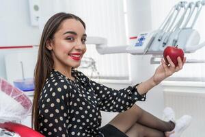 mooi jong mooi vrouw, model, meisje met rood lippen. meisje Holding een appel, lachend. dokter Bij tandarts kastje. detailopname foto