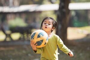 een jong meisje is Holding een voetbal bal in haar handen. ze is vervelend een groen overhemd en ze is opgewonden over spelen voetbal foto