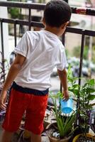 schattig 5 jaar oud Aziatisch weinig jongen is gieter de fabriek in de potten gelegen Bij huis balkon, liefde van zoet weinig jongen voor de moeder natuur gedurende gieter in planten, kind aanplant foto