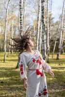 mooie vrouw in Oekraïense nationale traditionele kostuumkleren die in bos dansen foto