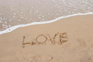 liefde belettering Aan de zanderig strand en zee water. foto