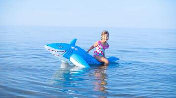 gelukkig meisje van Europese uiterlijk leeftijd van 7 zwemmen Aan een opblaasbaar groot haai speelgoed- in de zee.familie zomer roeping concept. kopiëren ruimte. foto