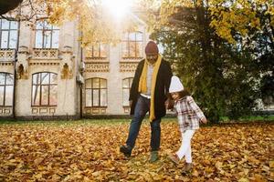 zwarte grootvader en kleindochter glimlachen terwijl ze samen wandelen in het herfstpark